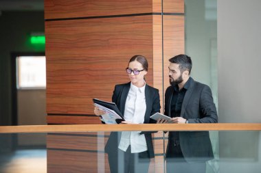 Takım elbiseli düşünceli genç iş adamları demiryolu kenarında durup belgeleri birlikte kontrol ediyorlar.