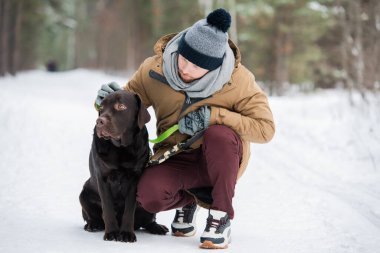 Gündelik kıyafet giyen genç adamın labrador av köpeğiyle dışarıda vakit geçirirken çekilmiş yatay bir fotoğrafı.