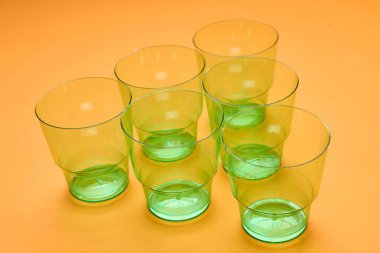 Horizontal high angle shot of six clean transparent green plastic cups on orange surface