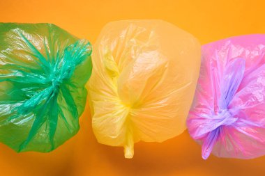 Horizontal from above conceptual shot of three multi-coloured plastic bags full of air on orange background