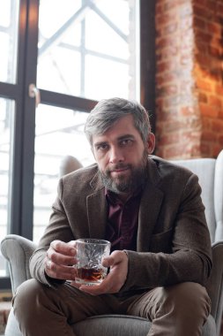 Ceketli, orta yaşlı bir adamın portresi rahat koltukta oturmuş, tek başına viski içiyor.