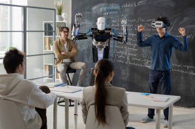 VR kulaklıklı çağdaş öğrenci sunum sırasında sınıf arkadaşlarının önünde otomasyon robotunun yeteneklerini gösteriyor.
