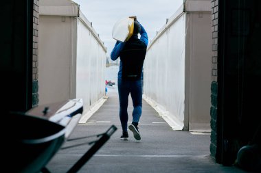 Kano eğitimi. Omuzunda kayık taşıyan ve bulutlu bir öğleden sonra suya doğru yürüyen tanımlanamayan erkek sporcunun arka görüntüsü