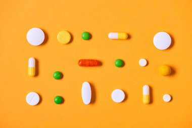 Multi-coloured medicaments on yellow background horizontal flat lay pattern shot