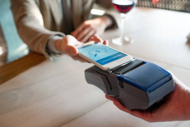Yatay yüksek açı, restoranda yemek parasını ödeyen tanınmayan bir adamın akıllı telefonda NFC kullanarak yakın plan çekimi.