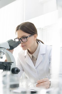 Vertical portrait young Caucasian medical scientist  wearing eyeglasses examining specimen using microscope in modern laboratory
