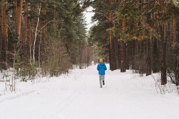 冬の森の中を走る青いジャケットの認識できない男のリアビュー — ストック写真