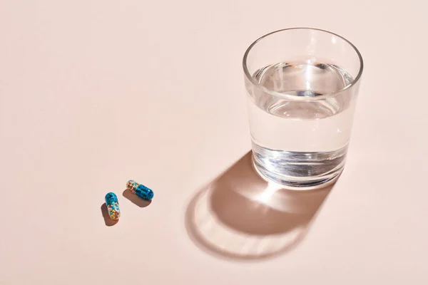 Két Kapszula Tabletták Üveg Vízzel Halvány Rózsaszín Felületen Vízszintes Lövés — Stock Fotó