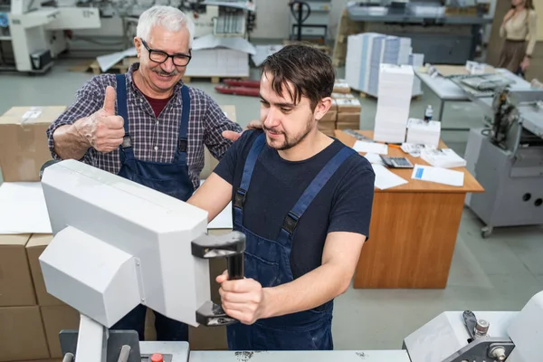满意的老年人在给印刷厂年轻的实习生操作机打分时表现得很出色 — 图库照片