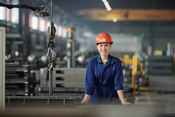 穿着工作服戴着防护头盔的快乐的年轻女性在现代工业工厂工作时看着你 — 图库照片