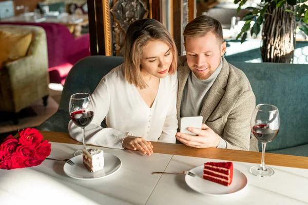 男子和女子坐在现代咖啡馆里用智能手机观看某样东西的横向高角镜头 — 图库照片