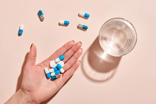 Különböző Gyógyszerek Női Kézben Egy Pohár Víz Halvány Rózsaszín Háttér — Stock Fotó