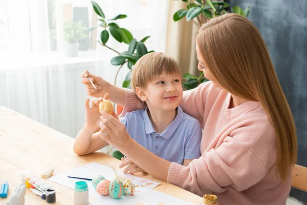 笑顔の息子は母親を見ている間に彼女は彼の手にイースターの卵を描く自宅で — ストック写真