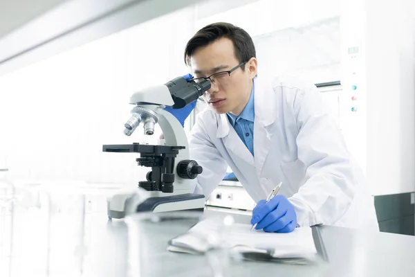 Asian Medical Scientist Wearing White Coat Examining Specimen Using Microscope — 图库照片