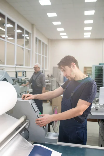 印刷機全体に立つ重大な若い労働者とコントロールパネル上のコピー量の選択 — ストック写真