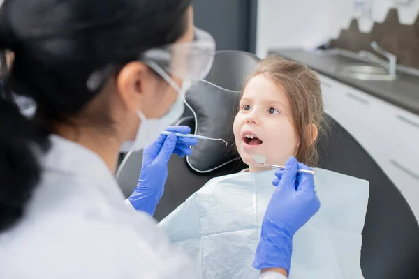 Κοριτσάκι Ανοιχτό Στόμα Κοιτάζοντας Τον Οδοντίατρο Προστατευτικά Ενδύματα Εργασίας Και — Φωτογραφία Αρχείου