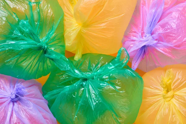 Green, yellow and violet plastic garbage bags full of air on orange background, horizontal flat lay conceptual shot