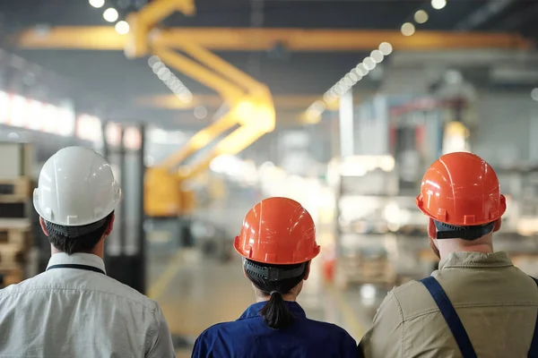 身着硬帽的当代工程师队伍在镜头前沿着大型工业厂房行进的背景图 — 图库照片