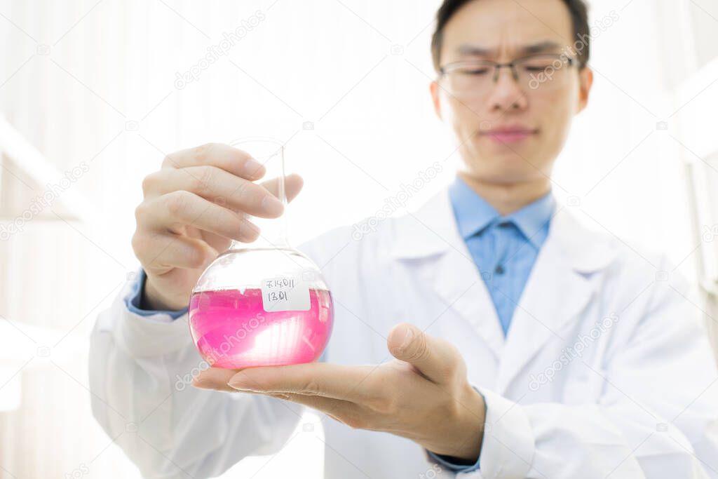 Horizontal portrait of young medical scientist wearing white coat and eyeglasses holding flask with pink liquid