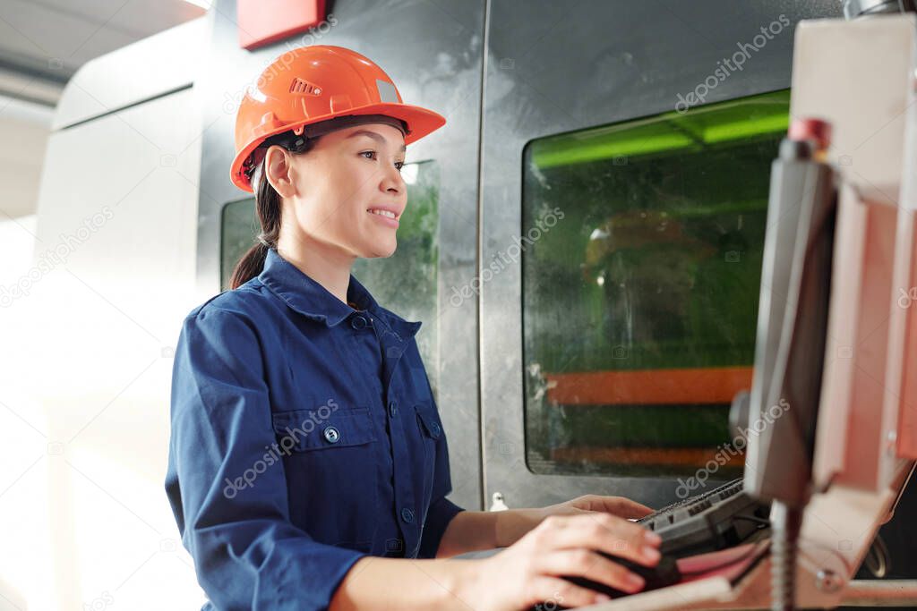 Young female engineer in helmet and workwear clicking mouse while looking at screen of monitor or control panel