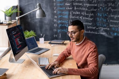 Gözlüklü çağdaş yönetici ofiste dizüstü bilgisayarın önünde oturuyor ve şifreli bilgiyle çalışıyor.