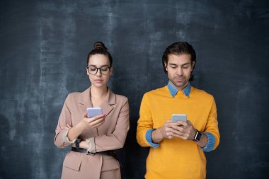 Küçük bir grup ciddi iş arkadaşı, akıllı günlük kıyafetleriyle karatahtanın yanında duruyor ve mobil cihazlarıyla kayıyorlar.