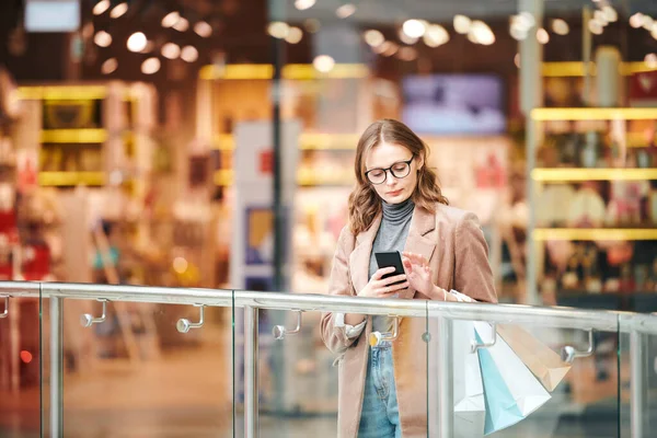 Poważna Młoda Kobieta Okularach Stojąca Balustradzie Sprawdzająca Smartfona Centrum Handlowym — Zdjęcie stockowe