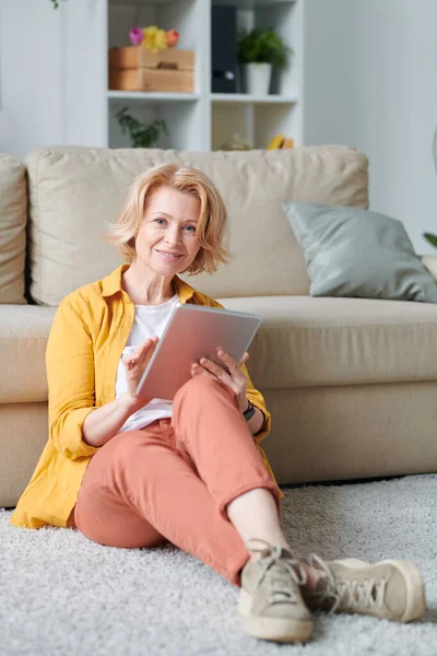 Blond Mature Female Casualwear Sitting Floor Couch Using Tablet While — Stock Photo, Image