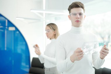 Çevrimiçi şemayı analiz ederken fütüristik tablet kullanan, modern gözlüklü yakışıklı bir gencin portresi.