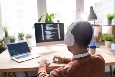 Bilgisayarın ve bilgisayarın önünde otururken kulaklıklı genç bir yöneticinin arka planı tuş takımının tuşlarına basıyor.