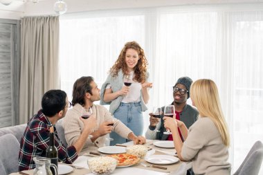 Kültürler arası beş mutlu arkadaş kırmızı şarap kadehlerini kaldırırken servis masasında oturacaklar.