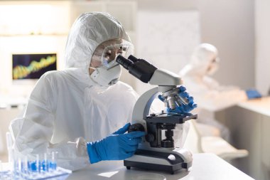 Bilimsel çalışmalar sırasında mikroskopta yeni kimyasal element ya da virüs moleküllerine bakan kadın bir laboratuar çalışanı ya da araştırmacı