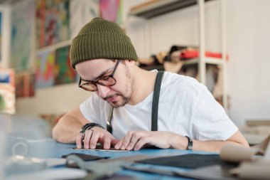 İş yerinde deri ya da süet ölçerken bereli ve tişörtlü profesyonel bir deri işçisi masanın üzerine eğiliyor.