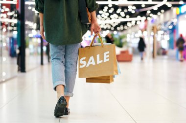 Alışveriş merkezinde yürürken elinde poşetlerle tanınmayan bir kadının arkadan görünüşü.