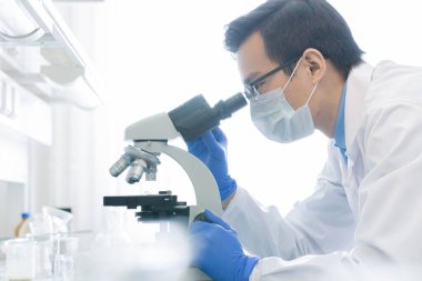 Genç Çinli bilim adamı veya koruyucu iş giyimi araştırmacısı Coronavirus 'la savaşmak için panzehiri geliştirmek amacıyla mikroskop altında yeni virüsler üzerinde çalışıyor.