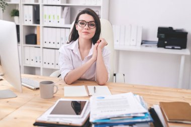 Gözlüklü güzel bayan müdürün portresi ahşap masada açık günlükle modern ofiste oturuyor.