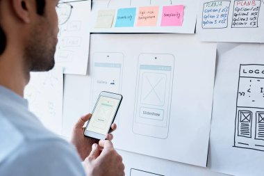 Görev tahtasında slayt gösterisi efekti tasarlarken akıllı telefon kullanan adamın omuz üstü görünümü