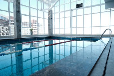 Şehir binalarına bakan panoramik pencereli kapalı yüzme havuzu