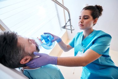 Hastanede hastaya oksijen verirken torba kapakçığı maskesi takan ameliyat eldivenli genç hemşirelerin görüş açısının altında.