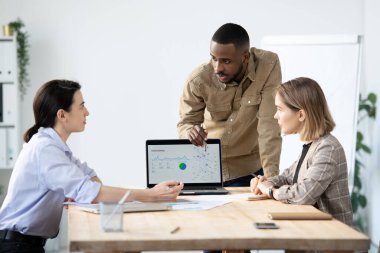 Meslektaşlarına ziyaretçi etkinliği hakkında veri sunarken dizüstü bilgisayar kullanan kendinden emin genç Afro-Amerikan hedef uzmanı