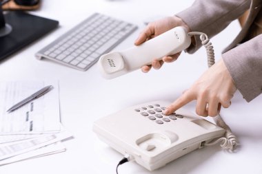 Genç ofis sekreterinin elleri telefon numarasını çeviriyor ve müşterilerden birini iş yerine çağırırken alıcıyı tutuyor.
