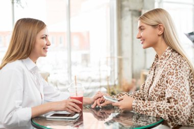 Alışveriş merkezindeki kafede oturup içki içen ve haberleri tartışan, akıllı, rahat giyimli iki genç bayan.