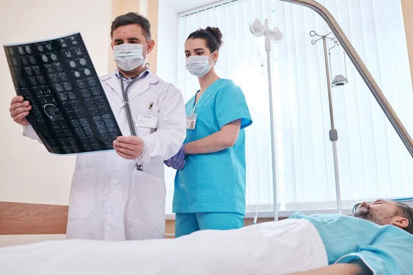 Médico Pensativo Enfermeiro Máscaras Cirúrgicas Analisando Imagem Raios Enquanto Paciente — Fotografia de Stock