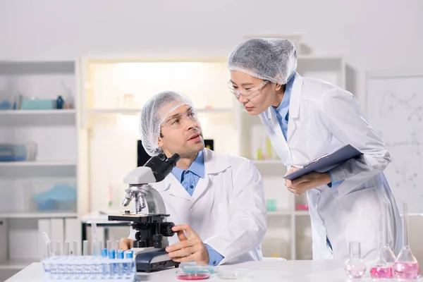 新しいワクチンを研究し ウイルスを研究しながら研究室でコンサルティングホワイトコートの2人の若い異文化科学者 — ストック写真