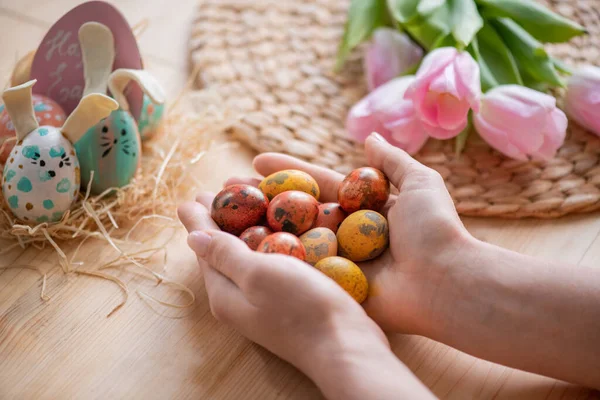在木制桌子上方拿着一把小小的复活节彩蛋 上面挂满鲜花和装饰性彩蛋的不明女子的近照 — 图库照片