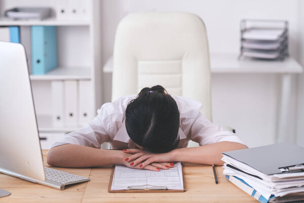 Puzzled brunette woman tired from work lying on table with application form while processing requests