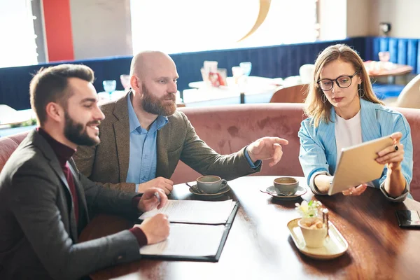 テーブルに座って 契約内容を話し合いながら同僚にタブレットの情報を示す眼鏡の現代のビジネス女性 — ストック写真