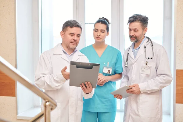 Reifer Arzt Laborkittel Hält Ordner Der Hand Und Zeigt Kollegen — Stockfoto