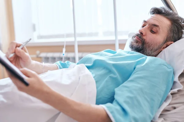 严重灰胡子患者躺在病床上 签署手术协议 — 图库照片