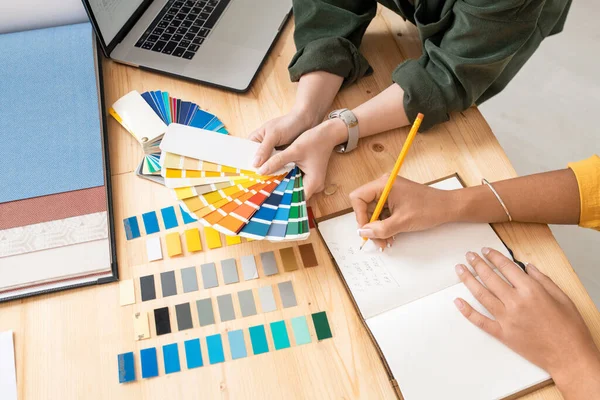 一位年轻的女设计师 当同事在新订单上边工作边做笔记时 她把彩色调色板放在桌子上 — 图库照片